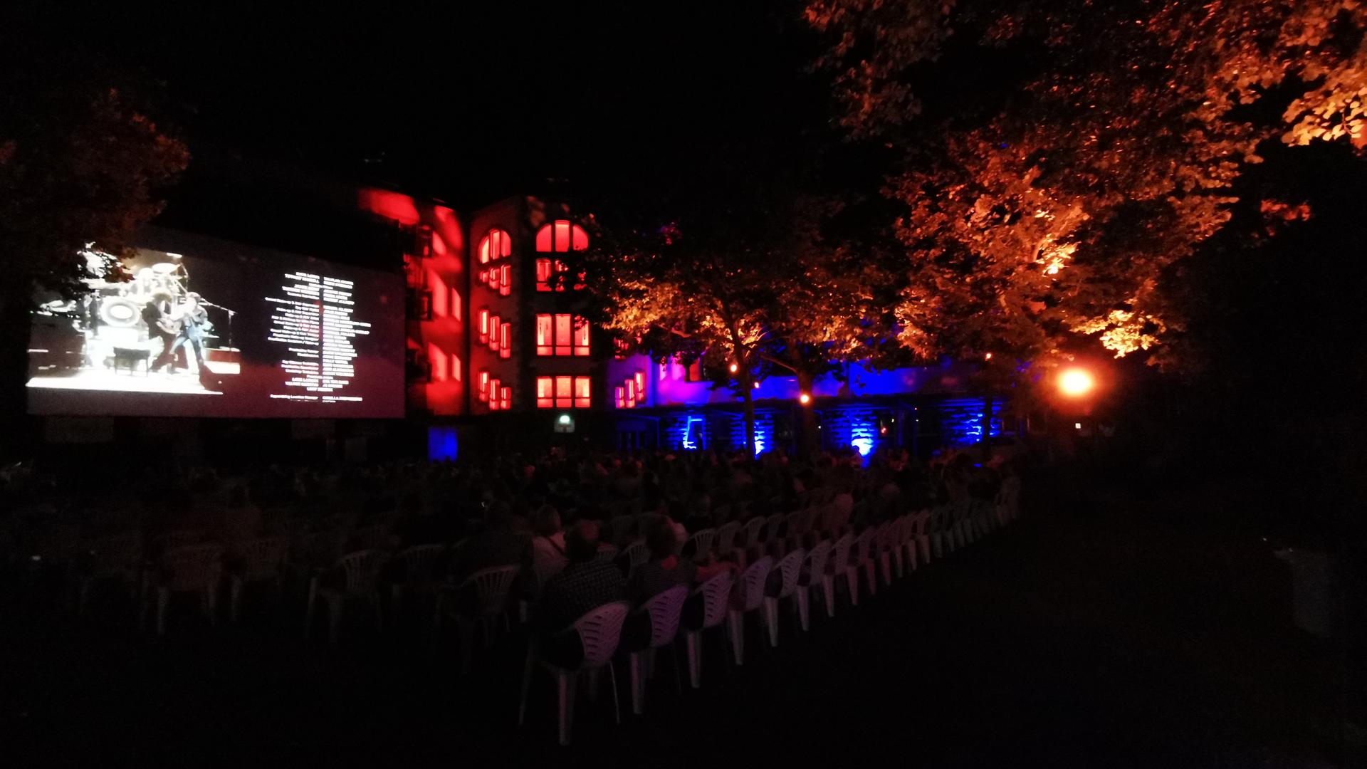 Kinoaufführung unter freiem Himmel mit Leinwand, Zuschauern unter Scheinwerfen in den Bäumen des Innenhofs im Kulturhaus Osterfeld in Pforzheim.