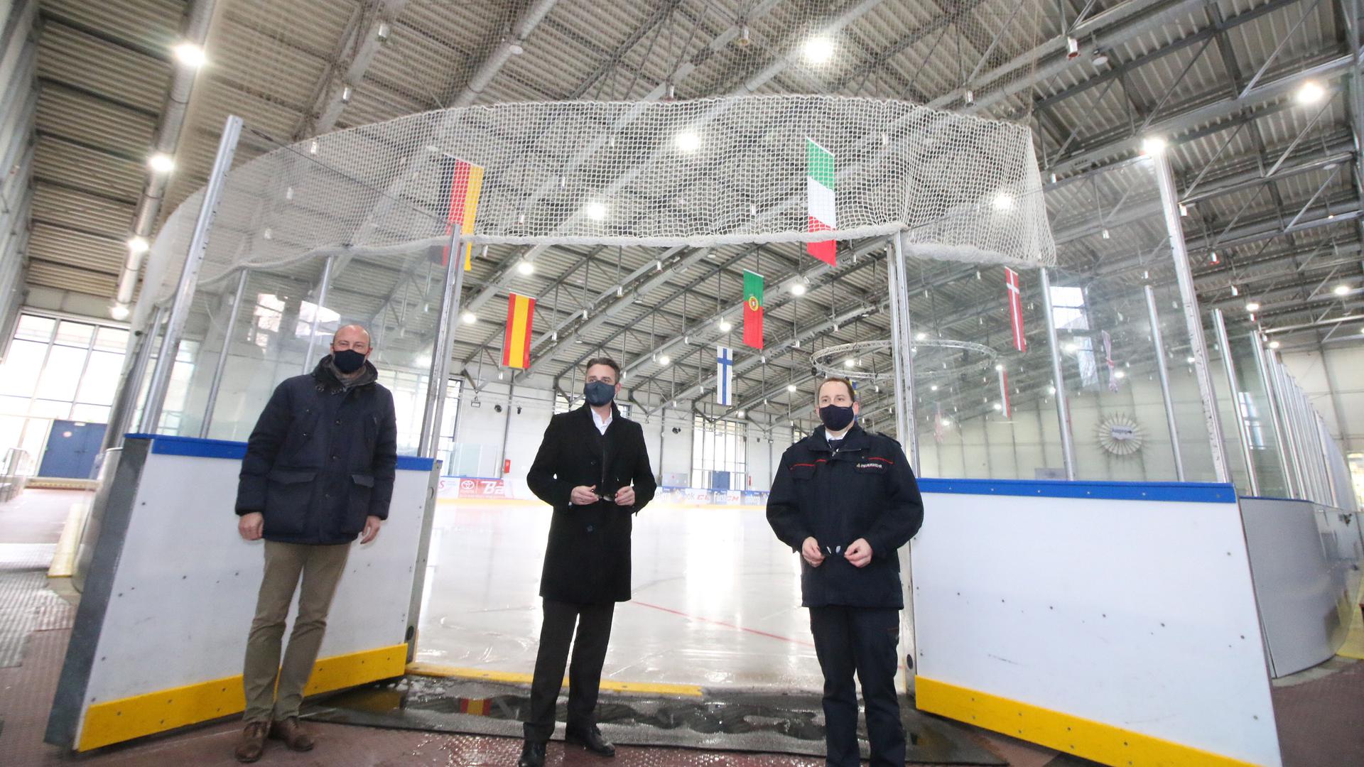 Drei Männer sehen nebeneinander vor einer Eisfläche, alle drei haben eine schwarze Maske auf.