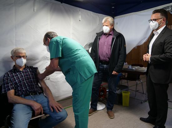 Vier Männer stehen in einem Zelt, einer wird geimpft.