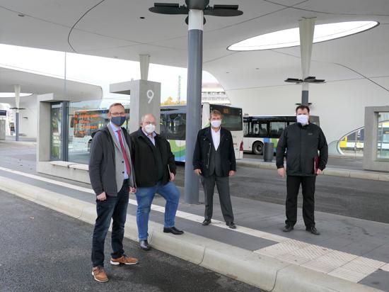 Vier Männer mit Masken stehen am Busbahnhof.
