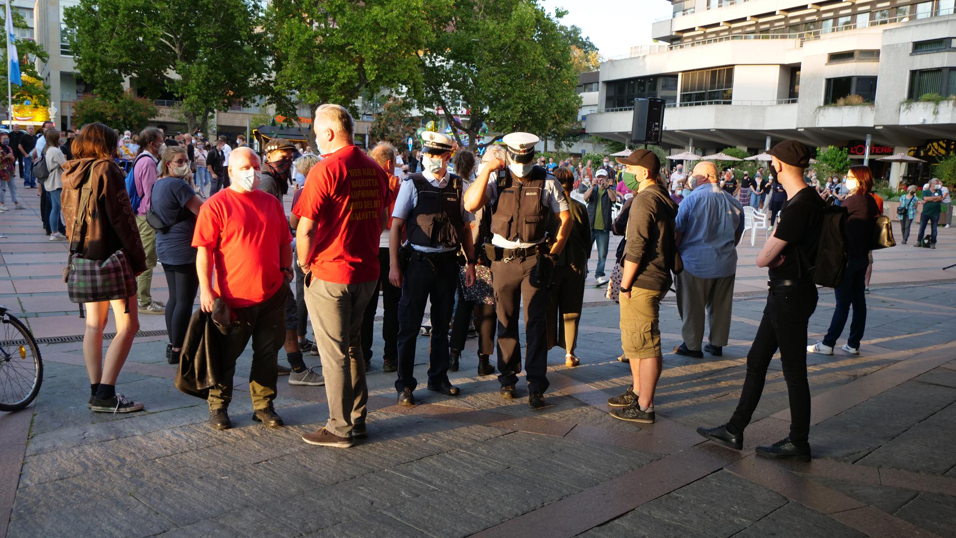 Kundgebung zur Lage der Flüchtlinge in Lesbos vor dem Rathaus Pforzheim mit Polizei und zwei Mitglieder von „Ein Herz für Deutschland“ in roten T-Shirts, die in Richtung Platz von Kundgebungsteilnehmern abgeschirmt werden. Ralf Fuhrmann blaues Hemd von links