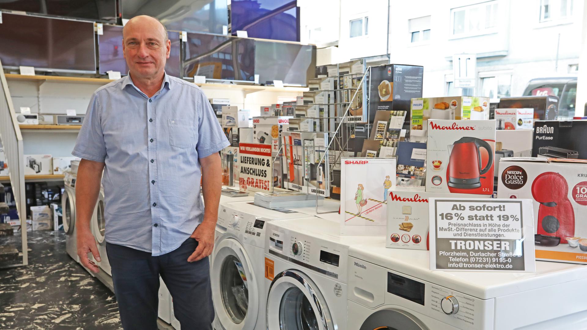 Bernhard Tronser steht im Elektrofachgeschäft vor Waschmaschinen. Rechts im Bild: ein Schild, das auf die Mehrwertsteuersenkung hinweist.
