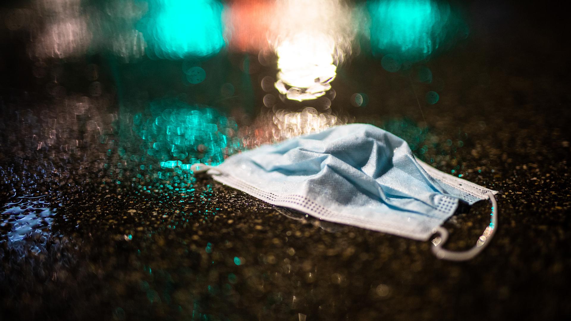 Ein Mund-Nasenschutz liegt am frühen Morgen im Regen auf der Straße.