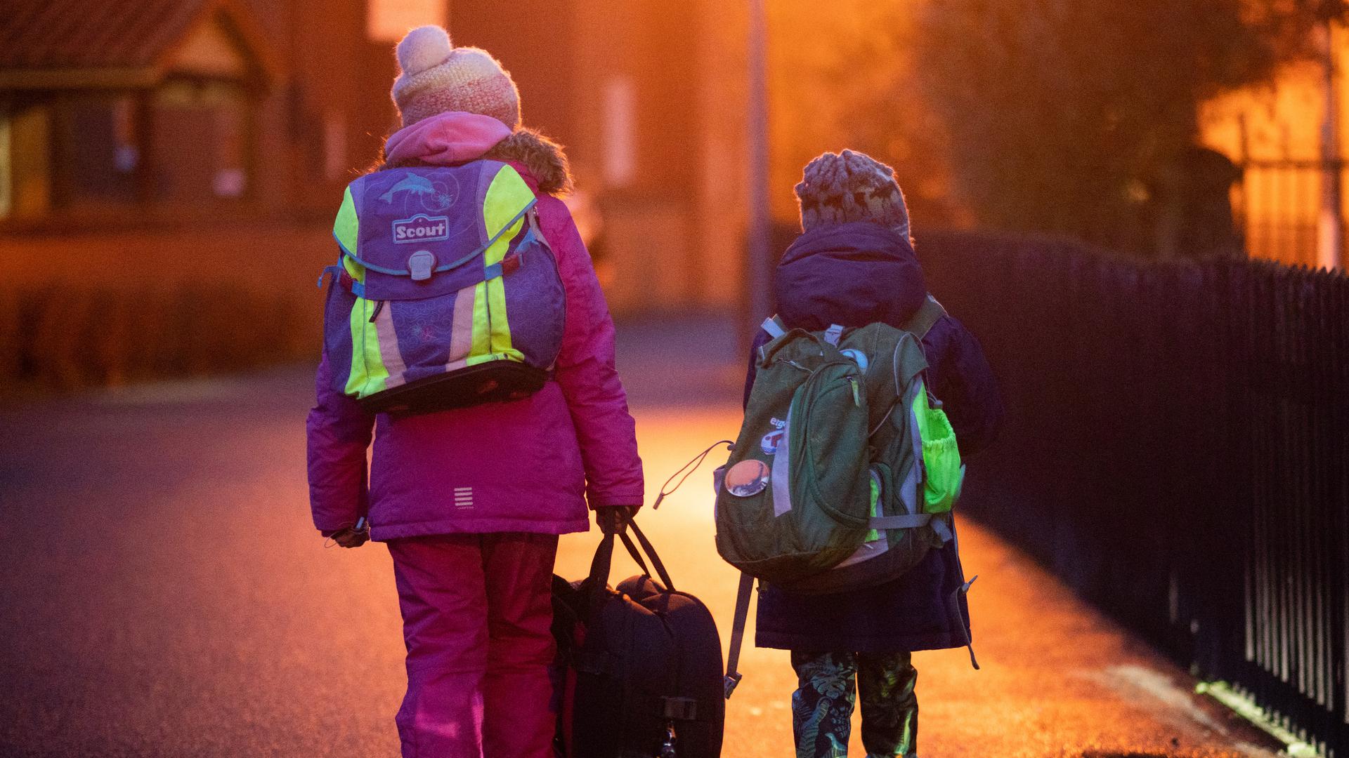 Zwei Schüler gehen am frühen Morgen auf dem Schulweg zu ihrer Grundschule.
