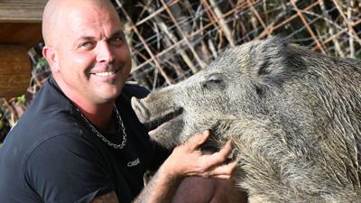 Dennis Renschler sitzt bei dem rund sechs Monate alten Wildschwein Friedrich in dessem Gehege.