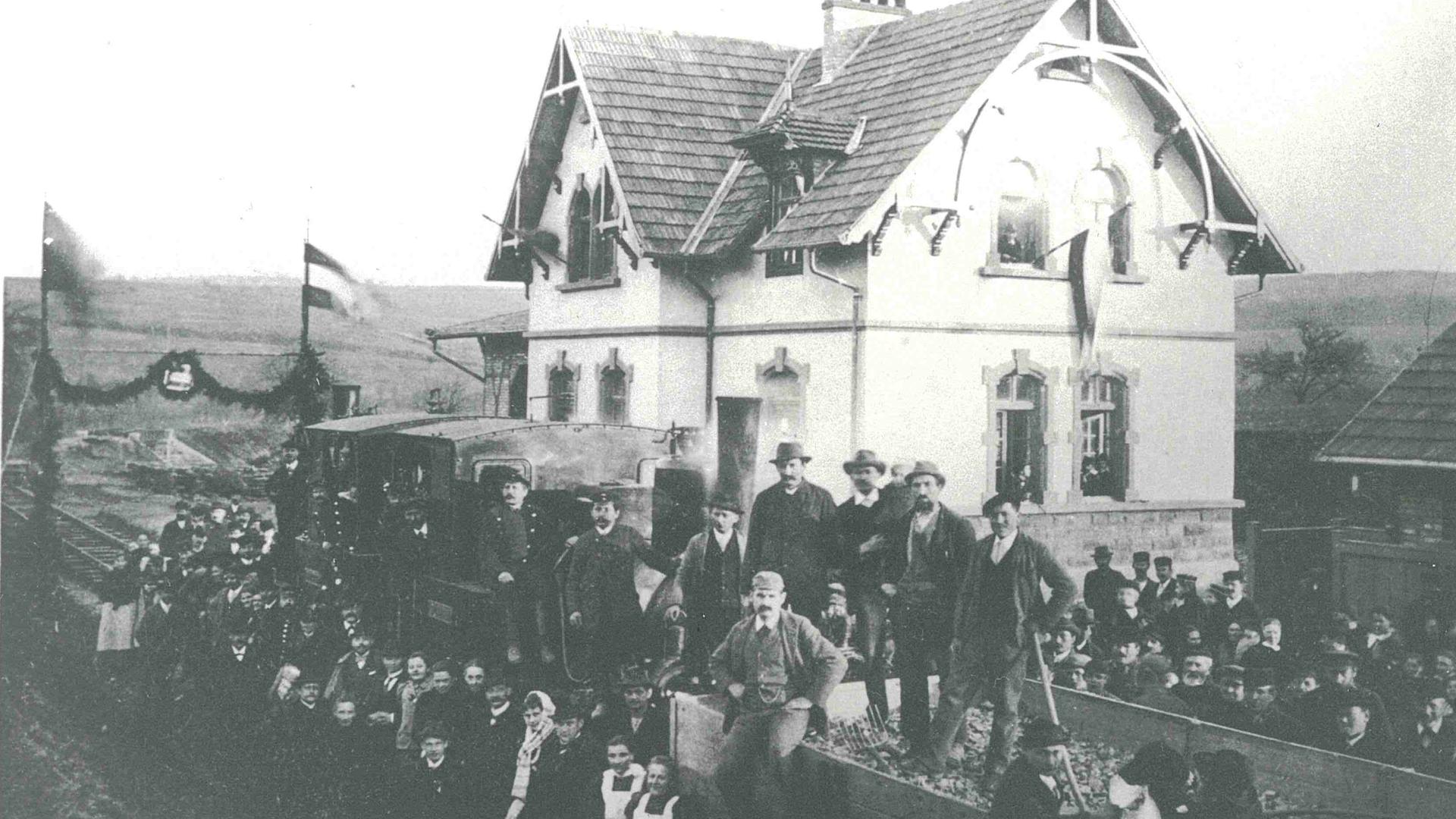 Bild des ersten Materialzugs in Ellmendingen. Rund um den Zug vor dem Bahnhof stehen zahlreiche Menschen.