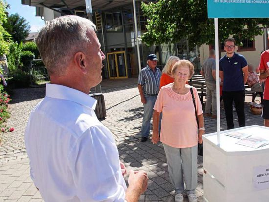 Heiko Genthner, der Bürgermeister von Königsbach-Stein, steht an einem Wahlstand und spricht zu Zuhörern.                             
