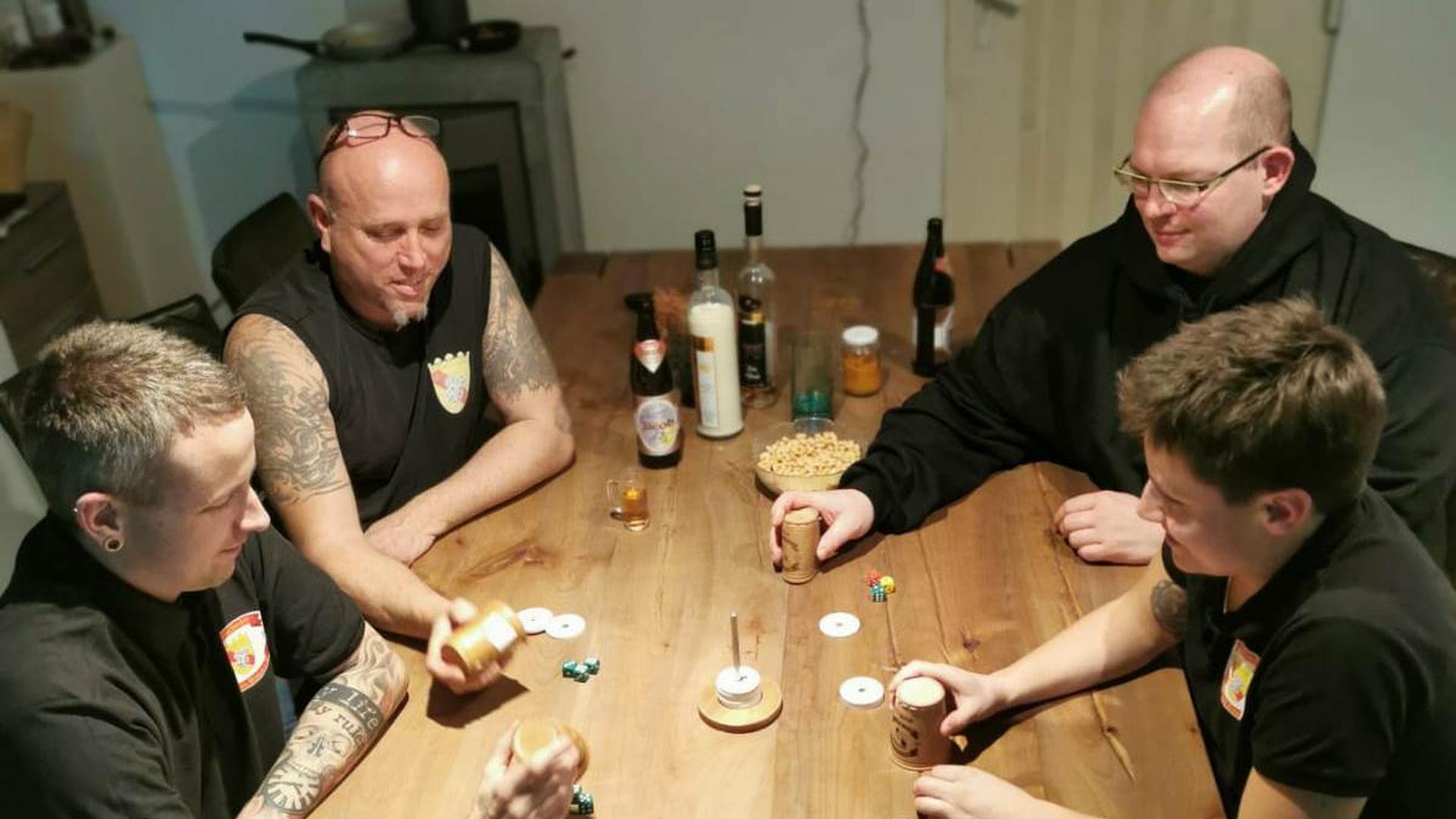 Vier Menschen sitzen am Tisch und spielen ein Würfelspiel.