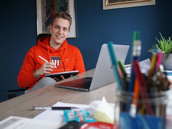Junger Mann vor Schreibtisch mit Laptop und Tablet