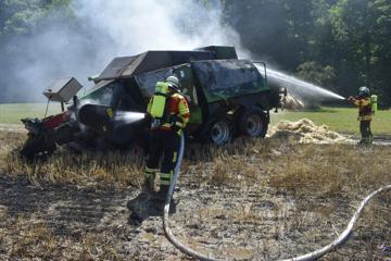 Einsatzkräfte löschen eine brennende Ballenpresse auf einem Feld bei Königsbach-Stein.