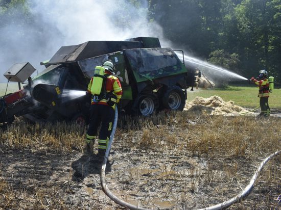 Einsatzkräfte löschen eine brennende Ballenpresse auf einem Feld bei Königsbach-Stein.