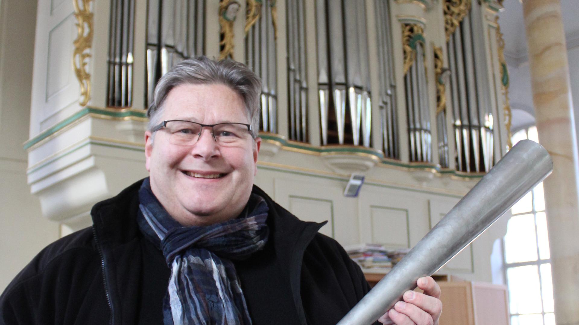 Bezirkskantor Bernhard Müller hält eine Spendenpfeife und steht vor der Orgel in der Neuenbürger Stadtkirche.