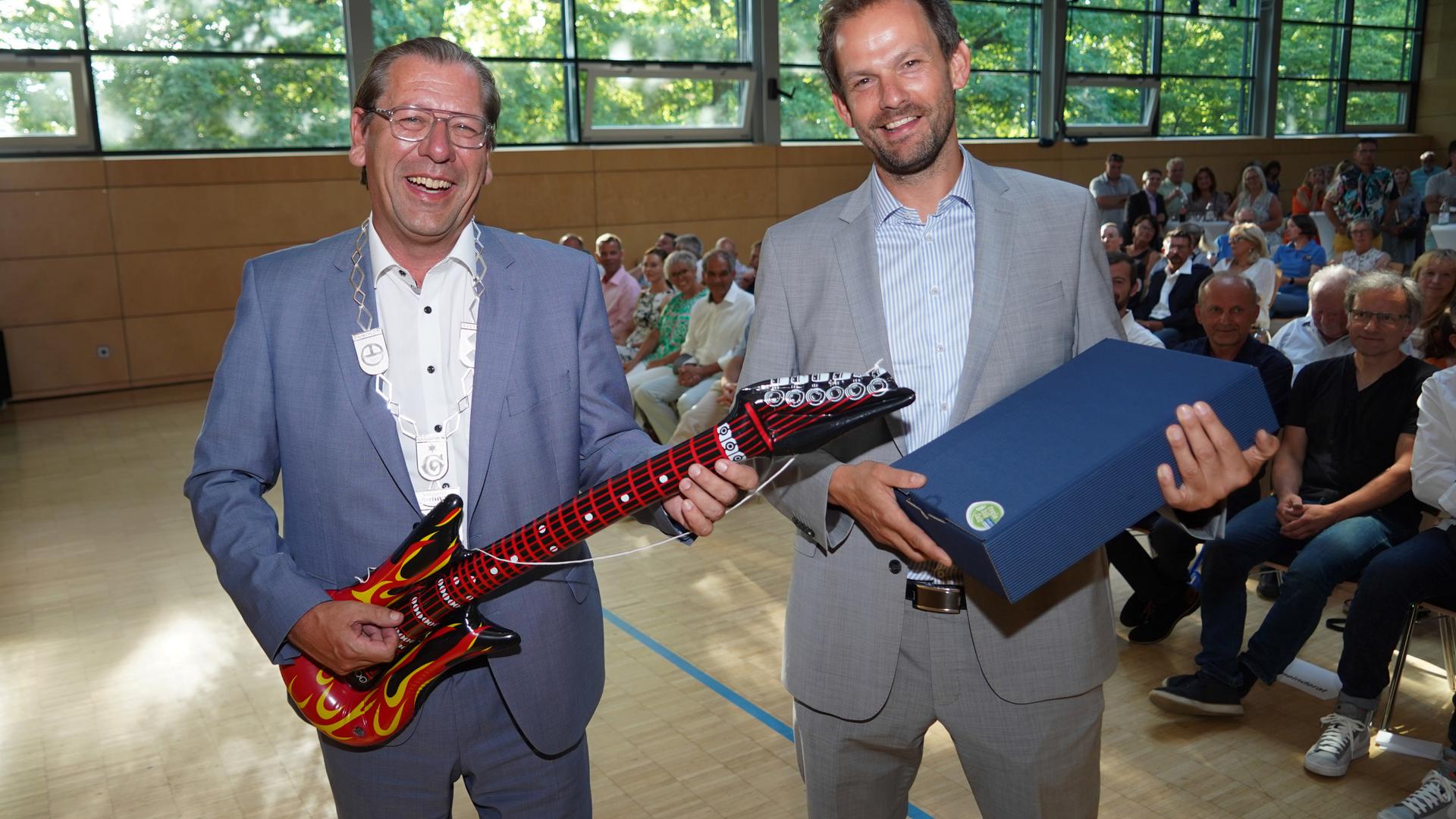 Ausgefallenes Antrittsgeschenk: Landrat Bastian Rosenau (rechts) überreichte eine Luftgitarre an den wiedergewählten Neulinger Bürgermeister Michael Schmidt.