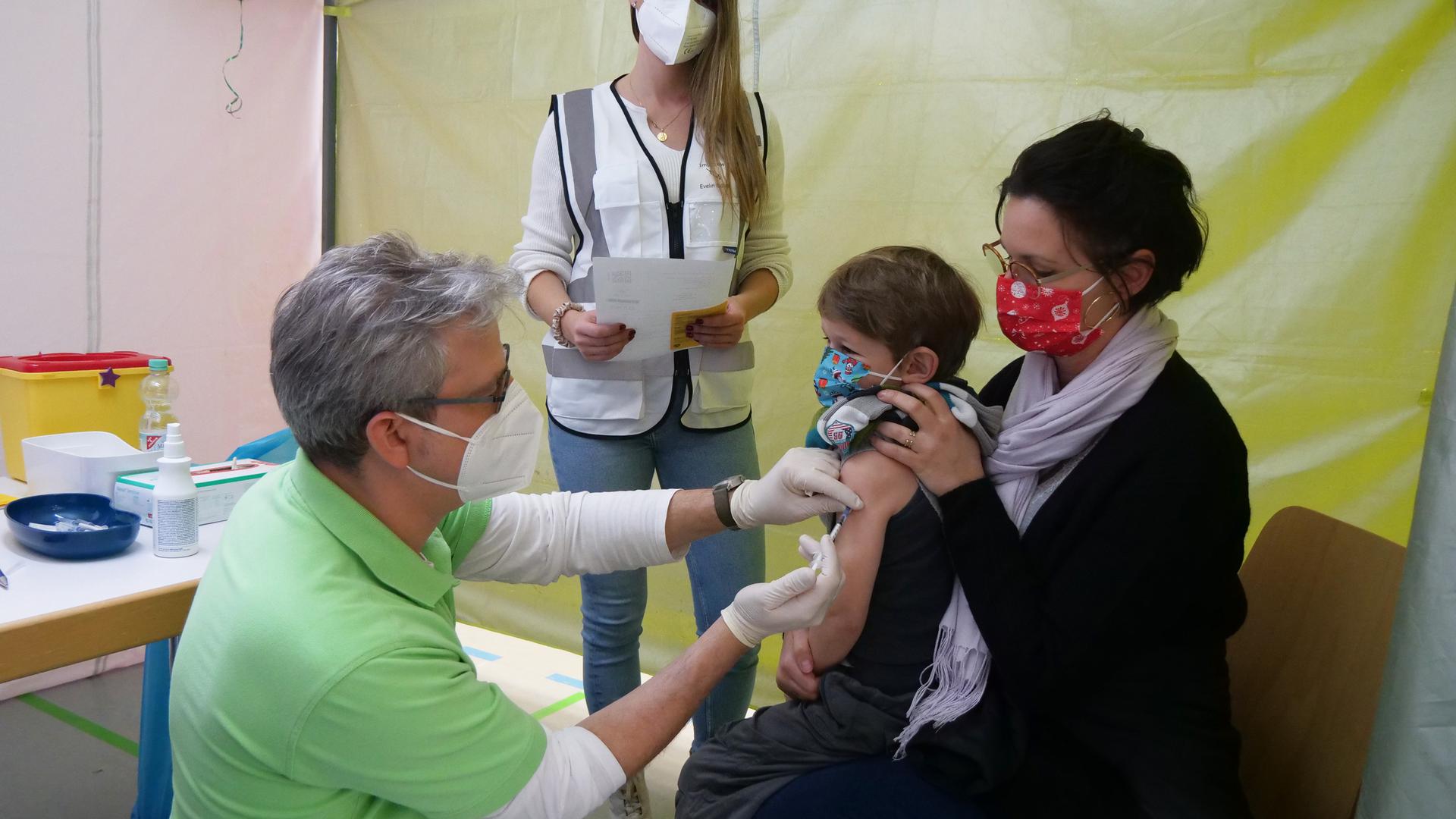 Joshua Glassmann impft einen Sechsjährigen im Beisein seiner Mutter. Evelin Eidner (2.v.l.) hat sich darum gekümmert, dass die Impfzelte in der Halle kindgerecht gestaltet waren