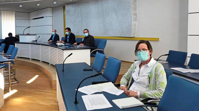 Ein Besprechungsraum. Im Vordergrund sitzt eine erschöpft wirkende Frau mit Mundschutz, es ist die Chefin des Gesundheitsamts. 