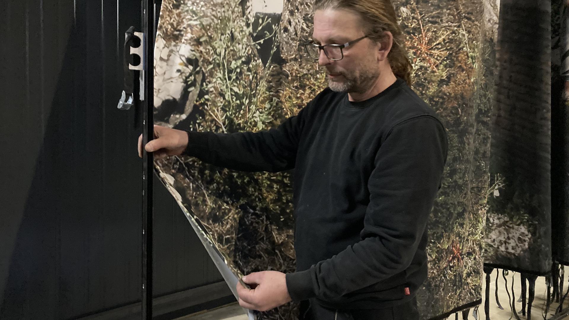 Jan Fehling zeigt wie der Stoff eines Panorama-Bildes in eine Keder-Schiene geschoben wird.