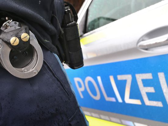 ILLUSTRATION - Ein Polizist mit Handschellen und einer Pistole am Gürtel steht vor einem Streifenwagen. Die bayerische Polizei fahndet derzeit nach 30 160 Verdächtigen oder Verurteilen. +++ dpa-Bildfunk +++