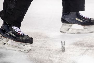 Eishockey: DEL, Eisbären Berlin - Iserlohn Roosters, Hauptrunde, 13. Spieltag, Mercedes-Benz Arena. Der Puck liegt auf dem Eis zwischen den Kufen zweier Schlittschuhe. (zu dpa: «Schwere Verletzung in der DEL: Mit Kufe Achillessehne durchtrennt») +++ dpa-Bildfunk +++