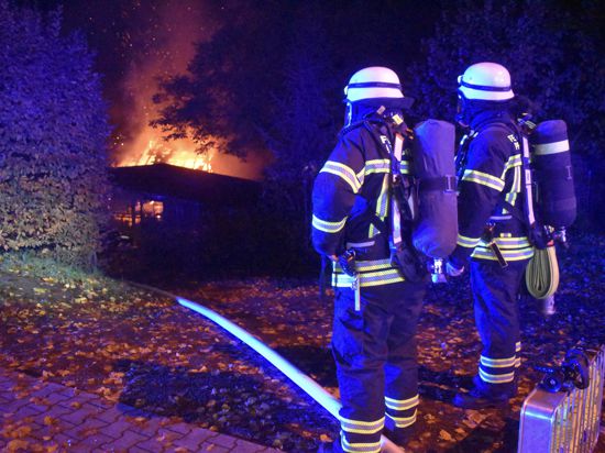 Zwei Feuerwehr-Einsatzkräfte beobachten den Brand einer Scheune in der Blumenthalstraße in Pforzheim.