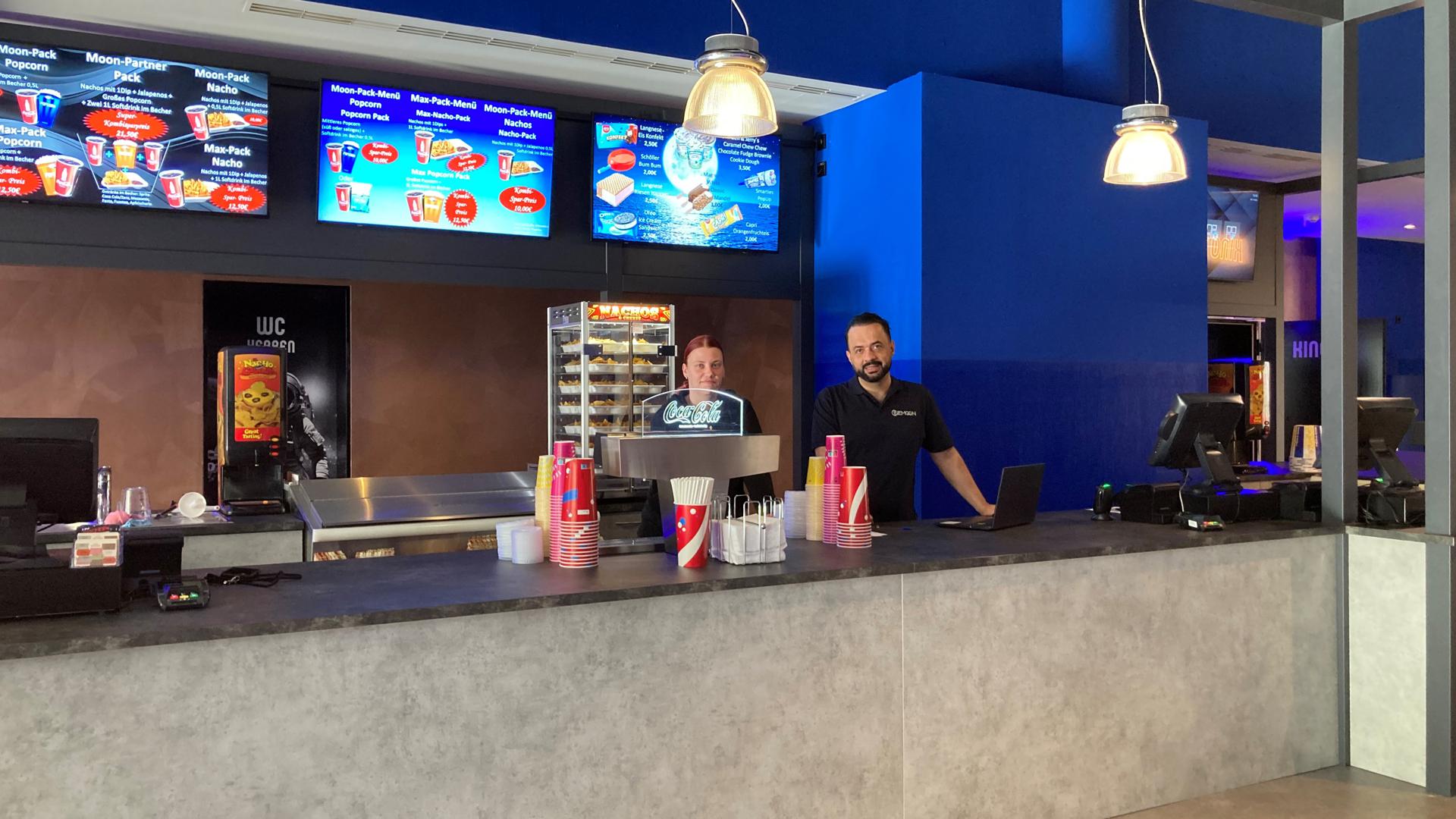 Snacks und Getränke können Besucherinnen und Besucher im Cinemoon bereits an einem Terminal im Eingangsbereich bestellen. Wer sich erst später entscheiden will, kann das auch an der Theke im ersten Stock tun. Hinter dem Tresen stehen Teamleiterin Bianca Stefer und Kino-Betreiber Vahid Shemshadian.