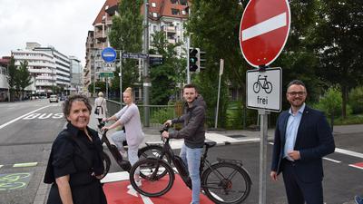 Zwei Personen auf dem Fahrrad stehen auf einem roten Radweg, zwei weitere Personen ohne Rad im Vordergrund