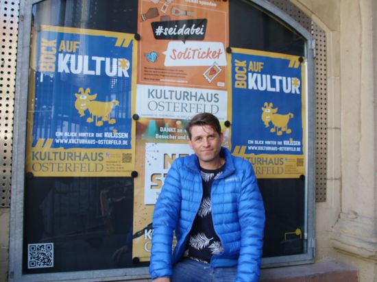 Ein Mann in blauer Jacke sitzt vor einem schwarzen Brett, auf dem Werbeposter mit den Slogans „Bock auf Kultur“ zu sehen sind. Bei dem Mann handelt es sich um den neuen Leiter des Kulturhauses Osterfeld Bart Dewijze.
