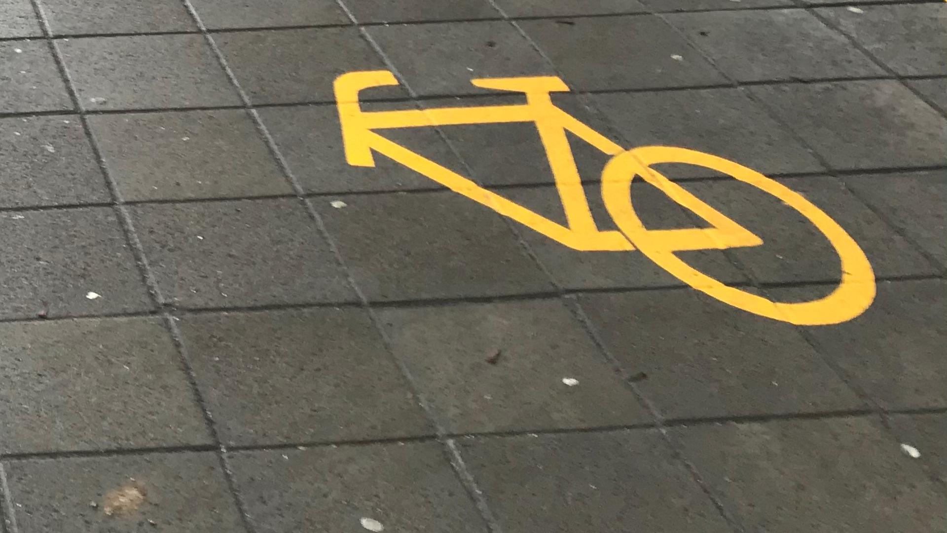 Ein Fahrradsymbol ist auf die Straße geklebt, dabei fehlt das Vorderrad.