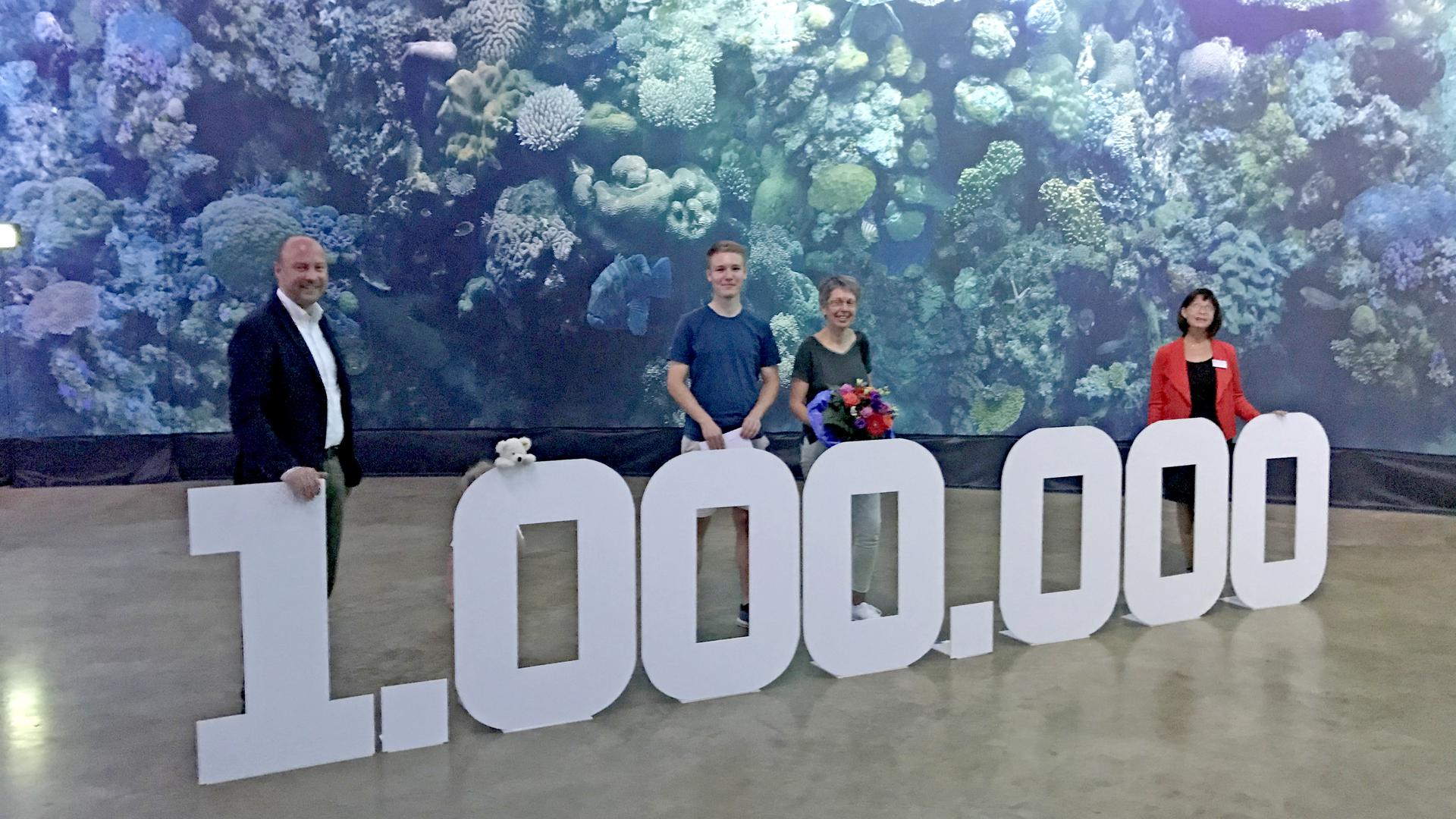 Mehrere Personen stehen hinter einer großen, aufgebauten 1.000.000. Im Hintergrund ist das Panorama mit dem Great Barrier Reef zu sehen.