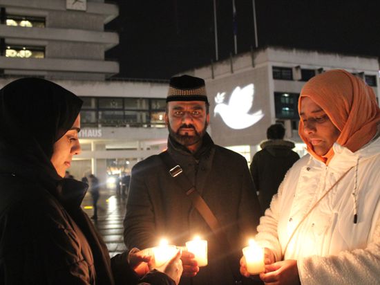 Drei Personen halten Kerzen in den Händen. Sie stehen vor dem Neuen Rathaus, auf das eine Friedenstaube projiziert ist.