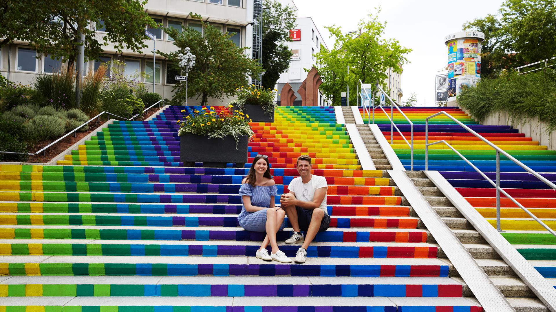 Linda Wendel und Bart Dewijze – das Künstlerduo The Artpole – auf der Treppe am Blumenhof, die durch ein Mitmachprojekt des Künstlerduos Farbe bekam.