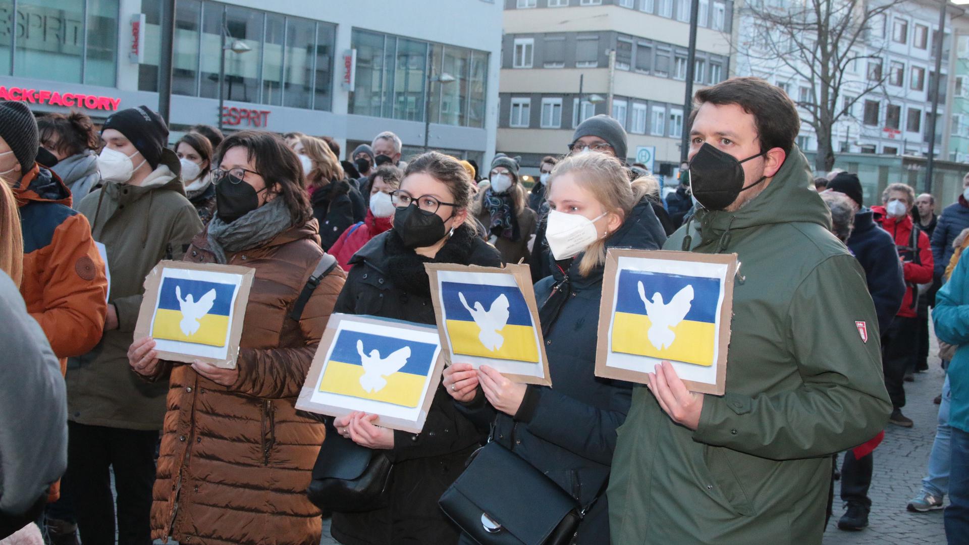 Demonstranten halten bei einer Friedenskundgebung für die Ukraine auf dem Pforzheimer Leopoldplatz ukrainische Flaggen mit Friedenssymbolen in Händen.