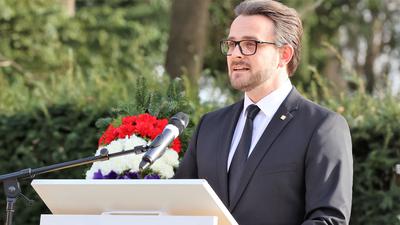 In dunklem Anzug vor einem großen Kreuz aus Stein: Pforzheims Oberbürgermeister Peter Boch (CDU) spricht am Dienstagnachmittag bei der offiziellen Gedenkveranstaltung der Stadt Pforzheim auf dem Hauptfriedhof
