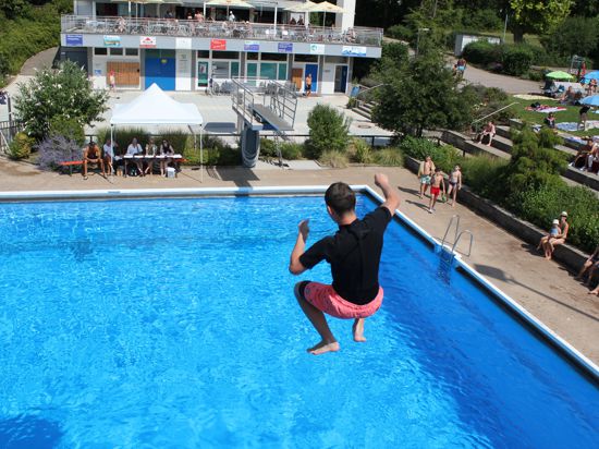 Jugendlicher springt im Freibad vom Sprungbrett ins Wasser.