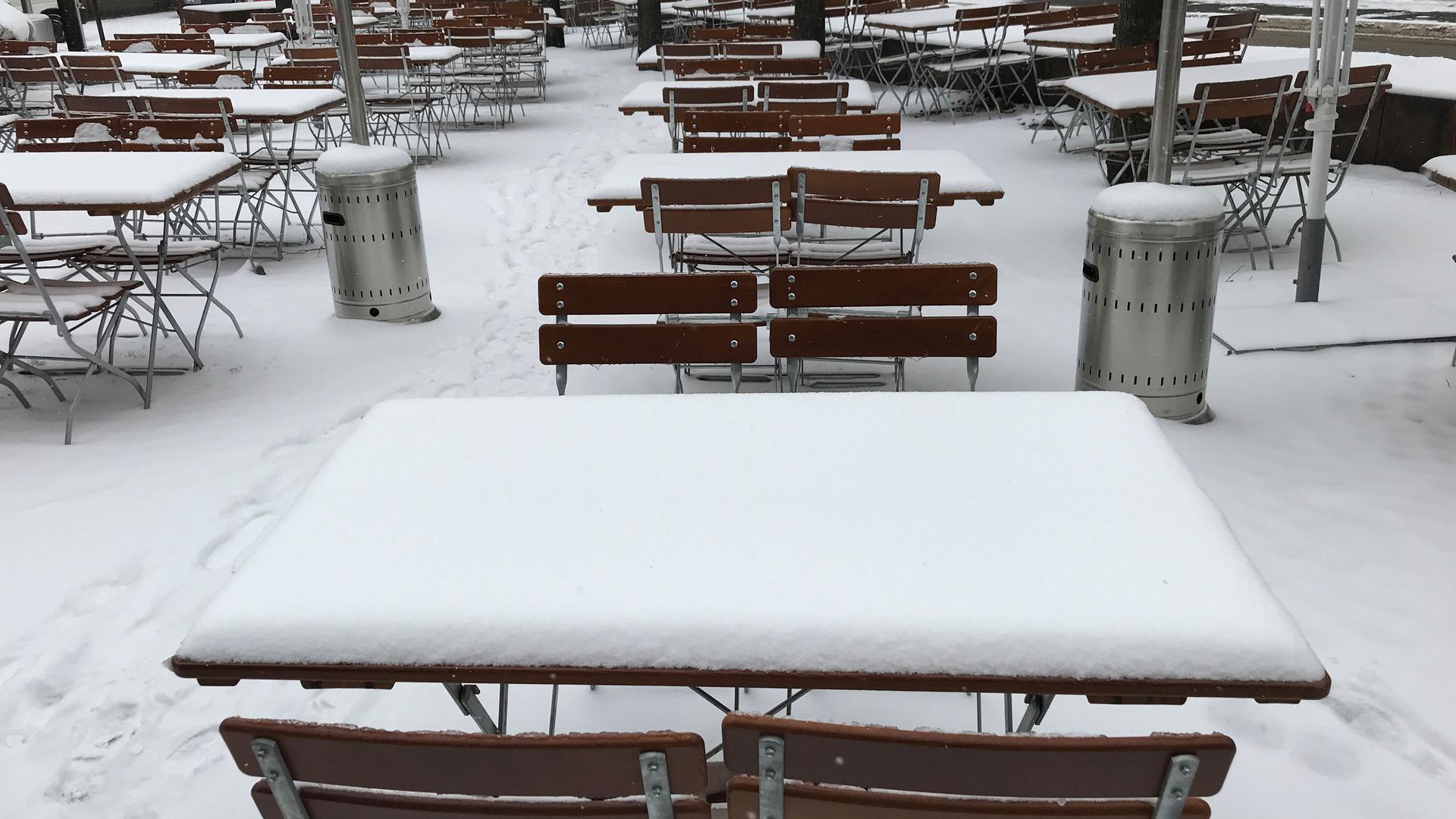 Mehrere Tische und Stühle, Außenbereich eines gastronomischen Betriebs, alles ist bedeckt von einer Schneeschicht.