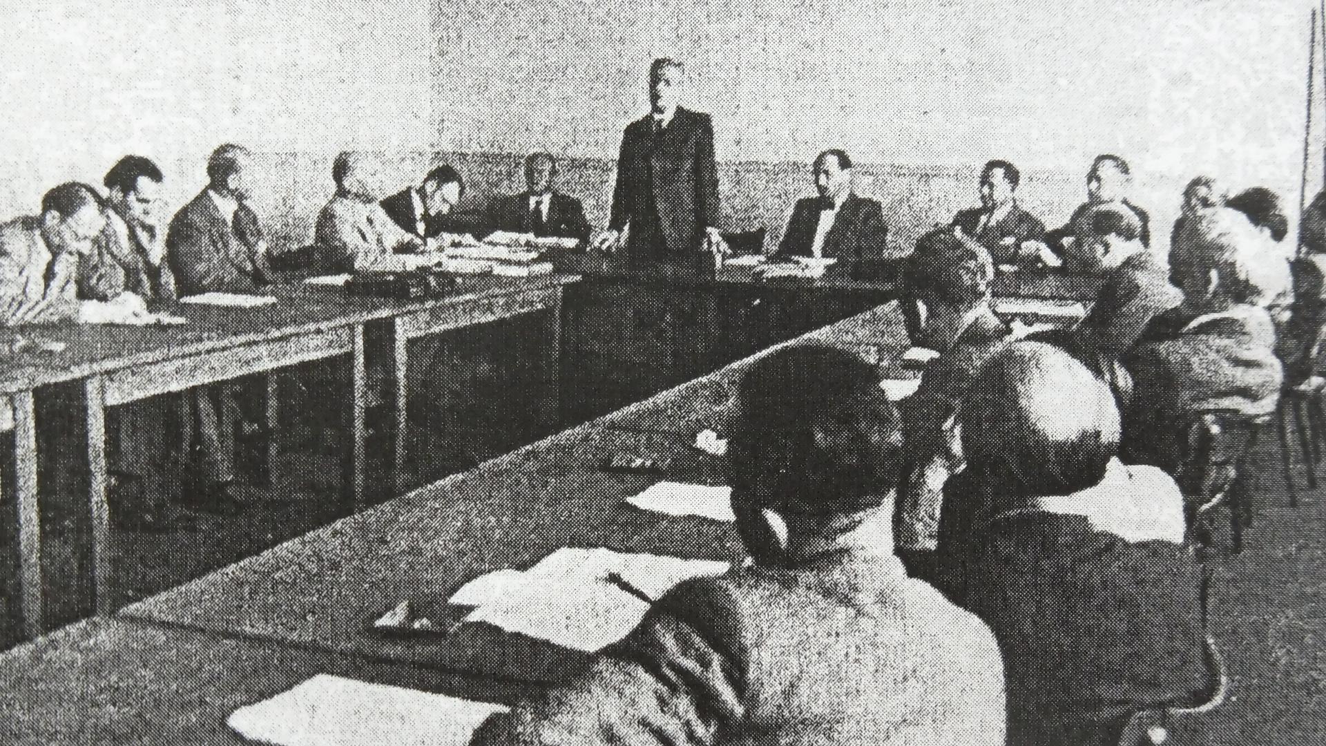 Mehrere Männer sitzen um einen Tisch, schwarz-weiß-Aufnahme