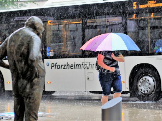 Eine junge Frau schützt sich in der Pforzheimer Leopoldstraße mit einem Schirm gegen den prasselnden Regen. Stoisch steht wie immer die Skulptur „Der Dicke“ 