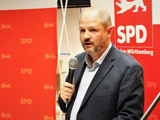 Ein Mann im Anzug steht mit Mikrofon vor einer rot-weißen SPD-Stellwand.