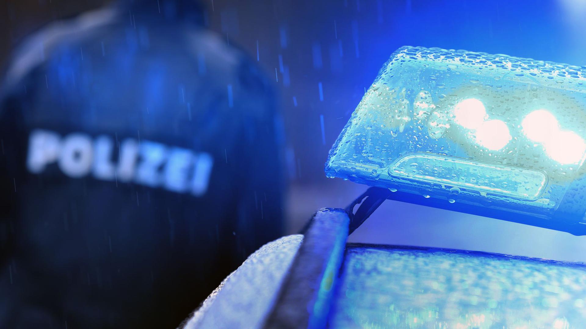 Ein Polizist steht vor einem Streifenwagen mit Blaulicht.