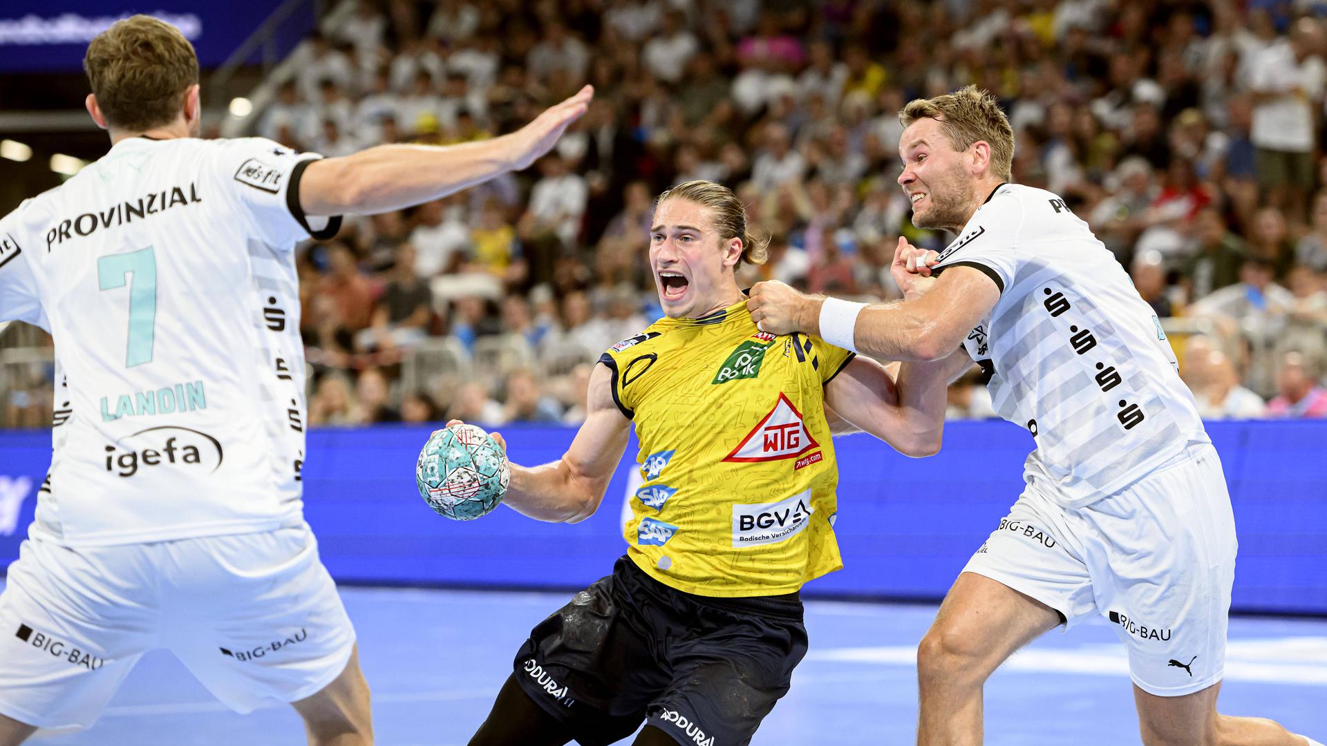 Juri Knorr (Mitte) von Rhein-Neckar Löwen hat den Ball und versucht sich im Handball-Super-Cup gegen den THW Kiel mit Magnus Landin Jacobsen (links) und Petter Overby zu behaupten.