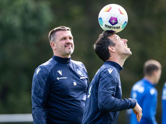 KSC-Trainer Christian Eichner balanciert im Training des Karlsruher SC vor den Augen seines Co-Trainers Zlatan Bajramovic einen Ball auf dem Kopf.