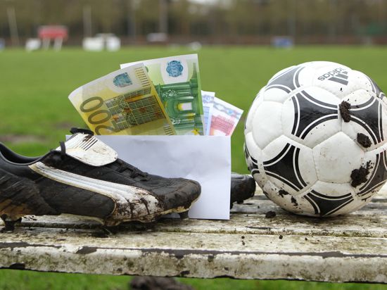 Ein Briefumschlag mit Geldscheinen steckt zwischen Fußballschuhen, die auf der Auswechselbank eines Sportplatzes stehen. Symbolbild/Symbolfoto Schwarzgeld im Amateurfußball. Winterhude Hamburg 