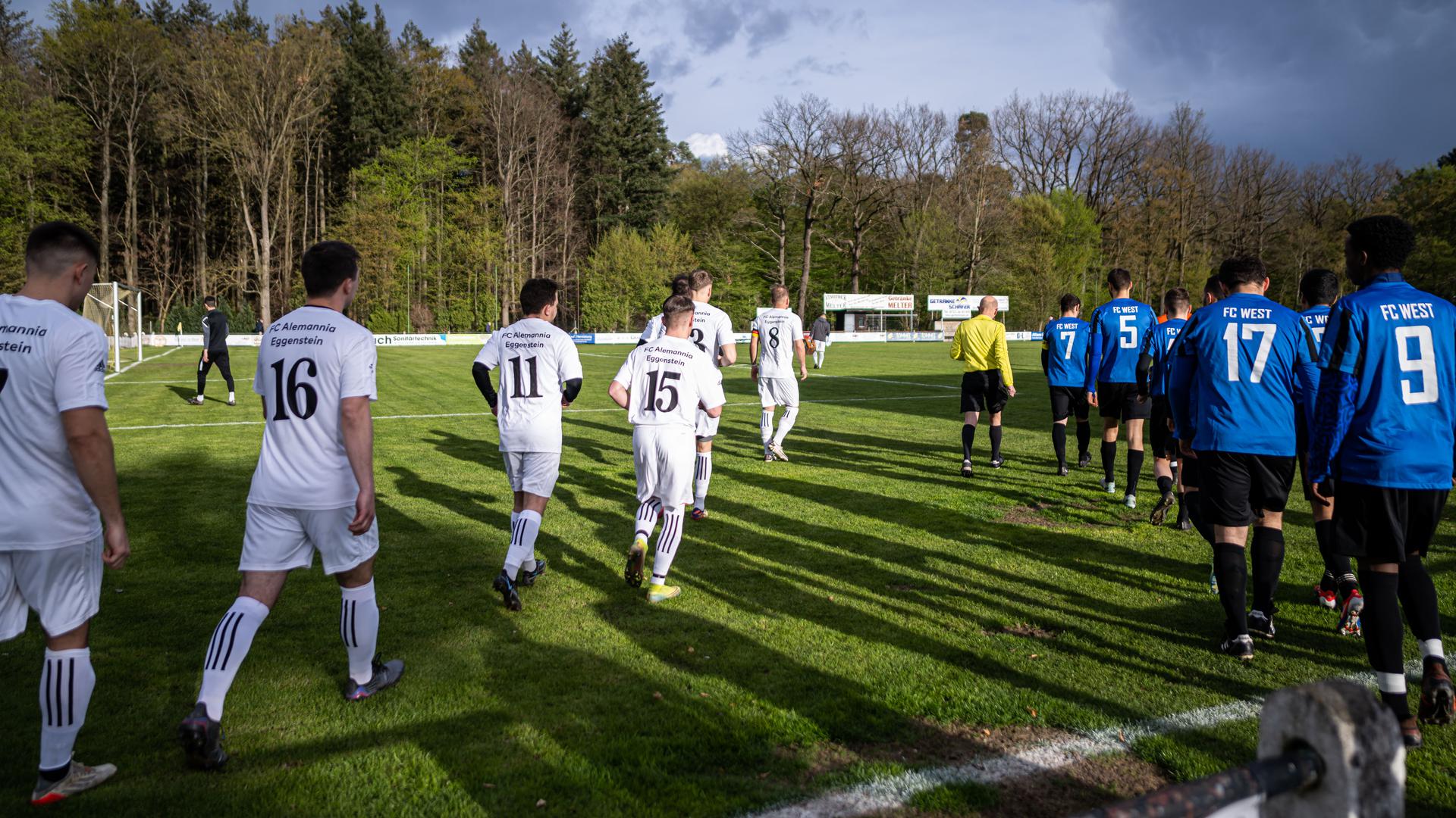 Die Fußballmannschaften des FC Eggenstein und des FC West laufen vor dem Spielbeginn auf das Spielfeld.