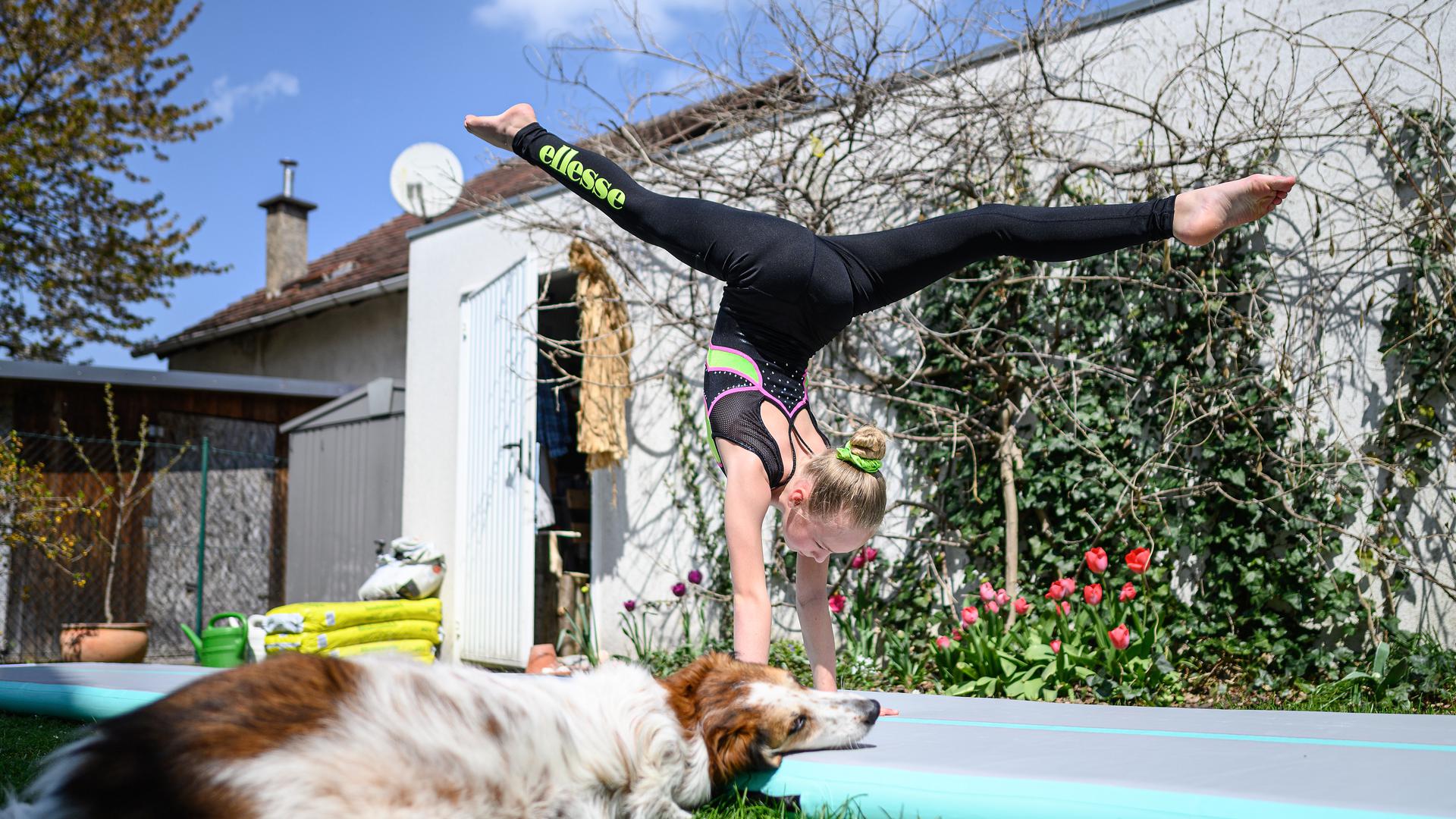 Jette Schroeder (KRK) trainiert im Garten des elterlichen Hauses auf einer AirTrack Matte. Hund Sally schaut zu.

GES/ Turnen/ Home-Training in Corona-Zeiten. 21.4.2021

