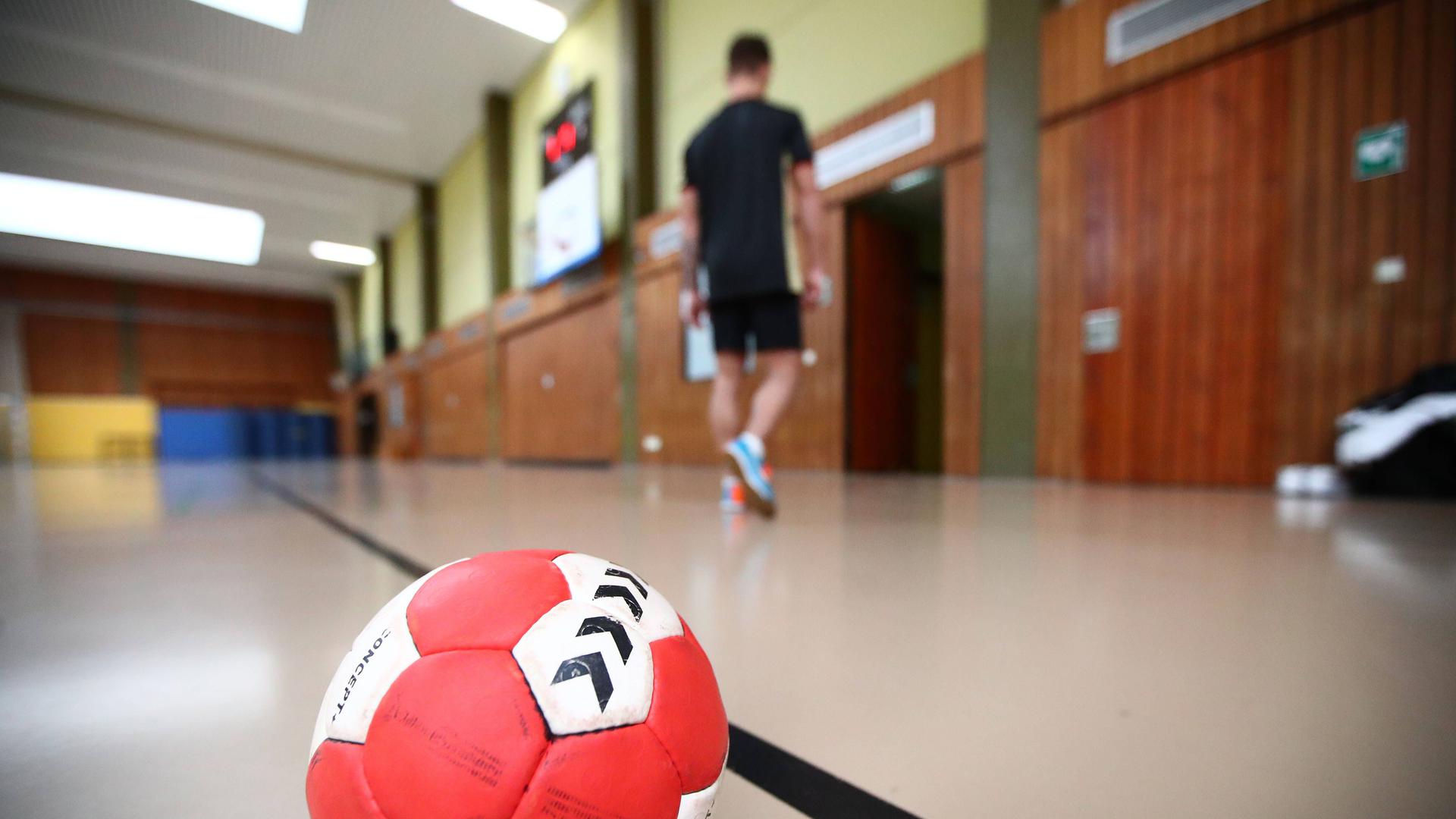 Warten auf die Wiederaufnahme des Trainings- und Spielbetriebs: Ein Handball liegt auf dem Spielfeld, während im Hintergrund ein Handballspieler die Halle verlässt 