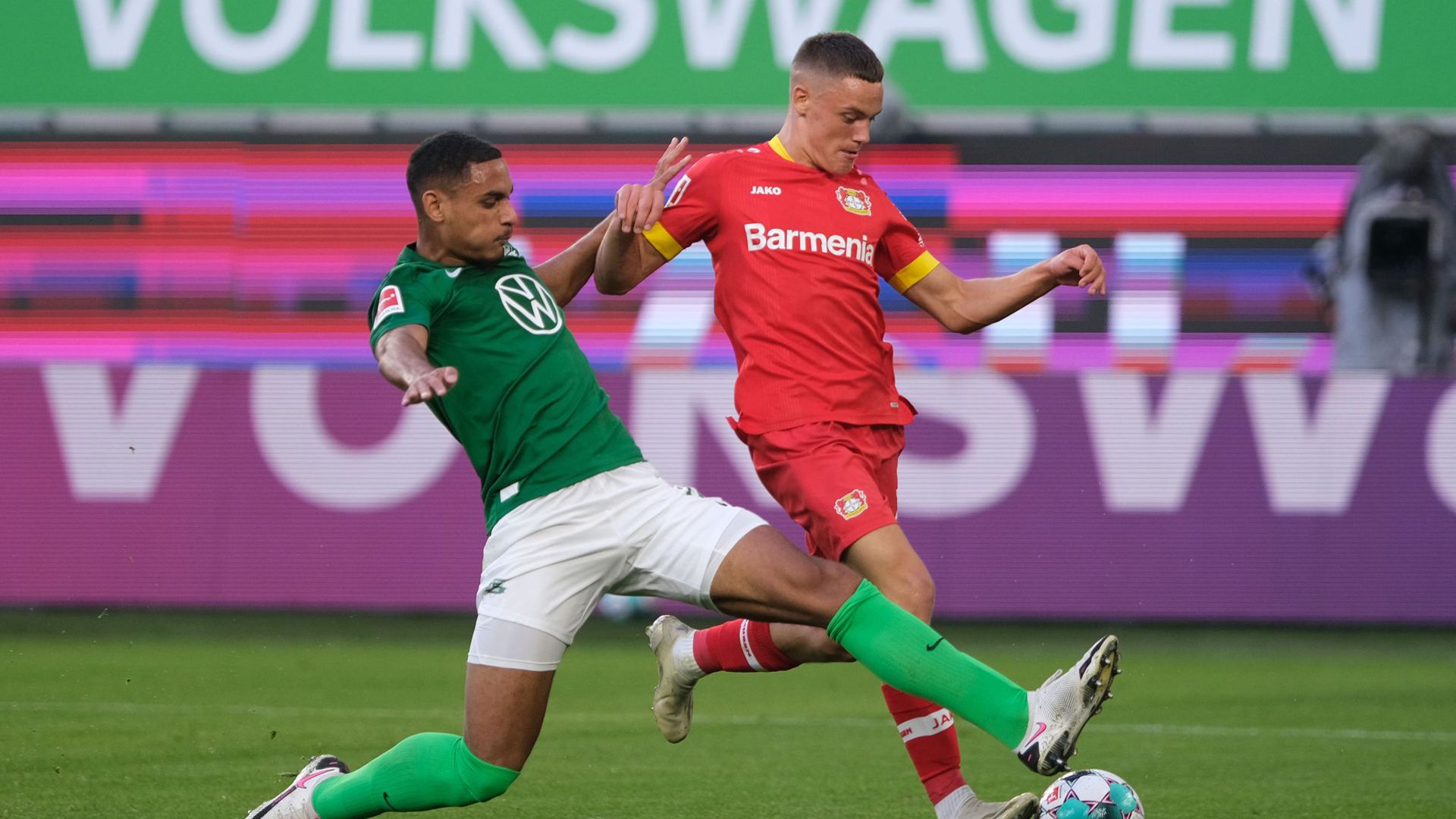 Wolfsburgs Neuzugang Maxence Lacroix (l) setzt gegen Leverkusens Talent Florian Wirtz zur Grätsche an.