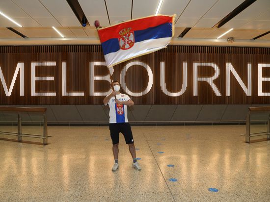 Ein Fan des serbischen Tennisspielers Novak Djokovic schwenkt in der Ankunftshalle des Flughafens Melbourne eine serbische Fahne.