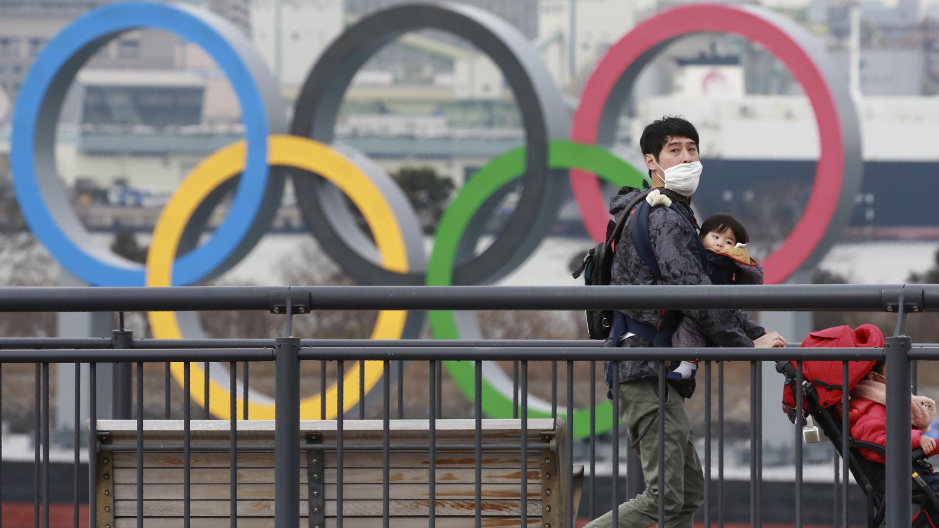 Olympia-Vorfreude? Nicht so sehr in Tokio. Das Bild zeigt einen Mann mit einer Gesichtsmaske und seinen Kindern vor dem Hintergrund der Olympischen Ringe. 